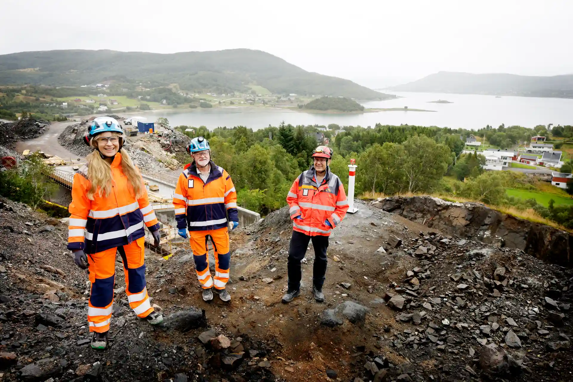 Bildet viser tre personer iført hjelm og verneklær i et anleggsområde. Bildeteksten sier, Her fra venstre: Daglig leder i Hålogalandsvegen AS, Fridhild Hjortdahl, Skanskas prosjektdirektør i OPS Hålogalandsvegen, Are Eliassen og prosjektsjef i Statens vegvesen, Reidar Johansen.